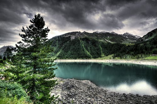 Kostenlos Gewässer Nahe Grünem Berg Unter Grauen Wolken Stock-Foto