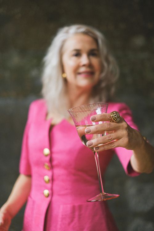 Free Senior woman in pink dress holding wine glass with focus on jewelry. Elegant lifestyle moment. Stock Photo