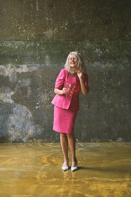 Free Cheerful senior woman in vibrant pink suit joyfully dancing in an industrial setting. Stock Photo