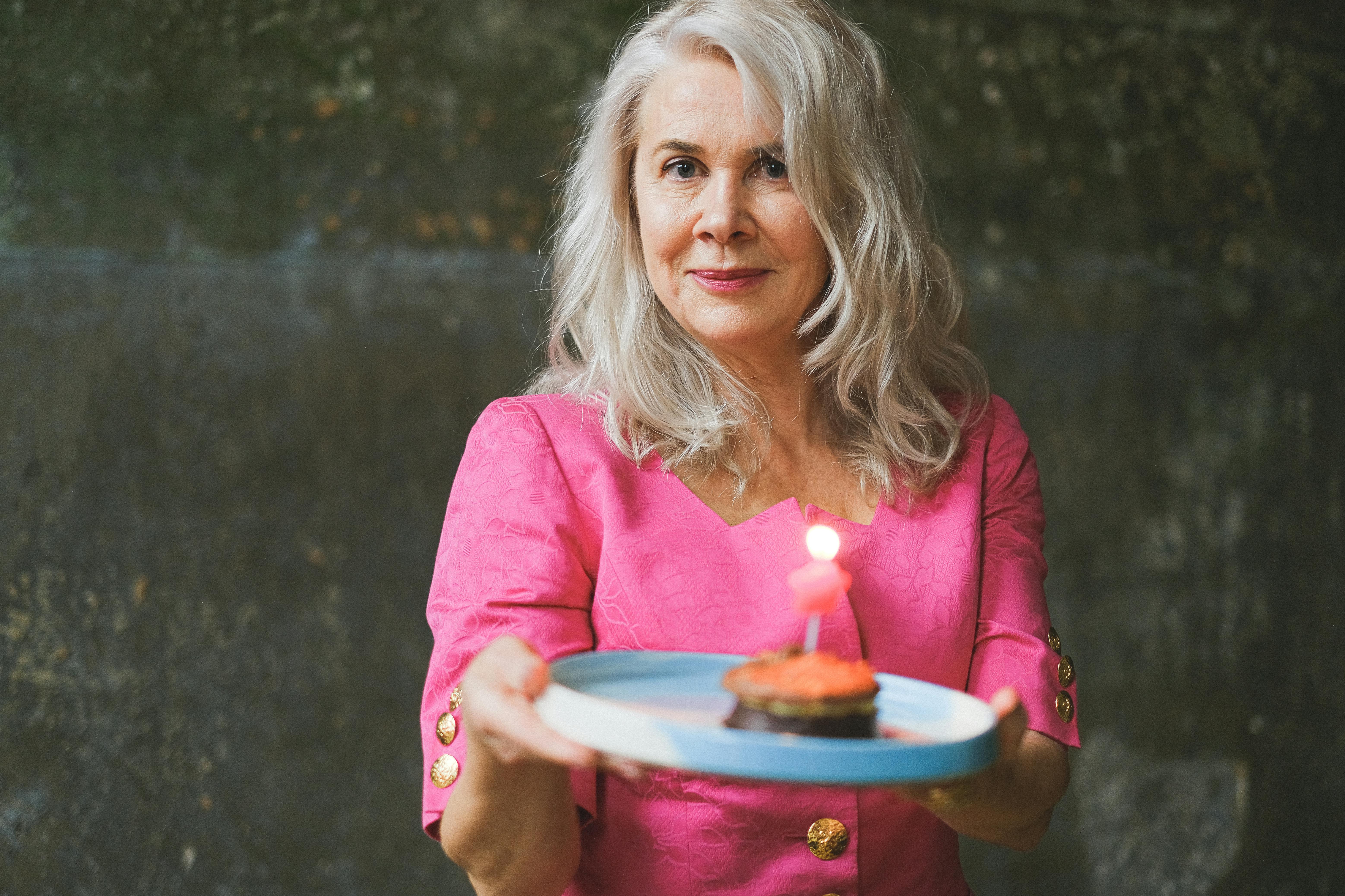 photo of a woman with gray hair holding a plate with a birthday cake