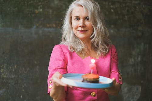 Photo of a Woman with Gray Hair Holding a Plate with a Birthday Cake