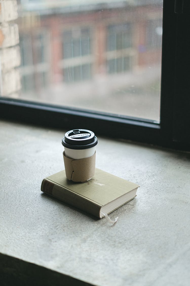 Plastic Coffee Cup On Book On Windowsill