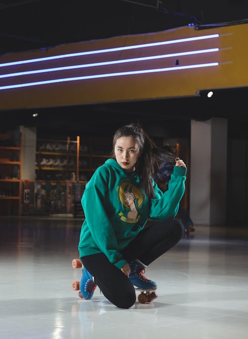 Woman in Green Hoodie and Black Pants Wearing Roller Skates Sitting on Floor