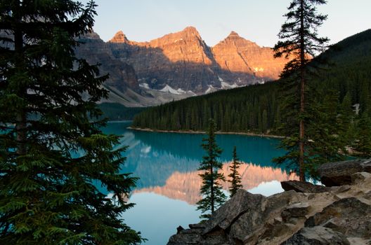 Sunrise at Moraine Lake with mountain reflection and dense forest.