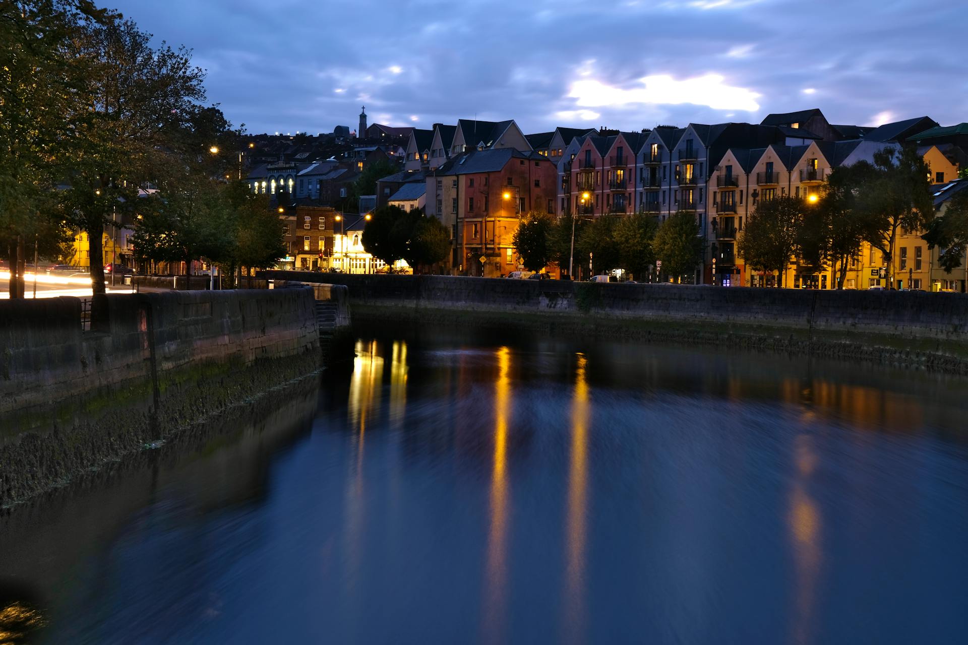 Nighttime view of Cork city's illuminated canal and buildings, reflecting lights beautifully.