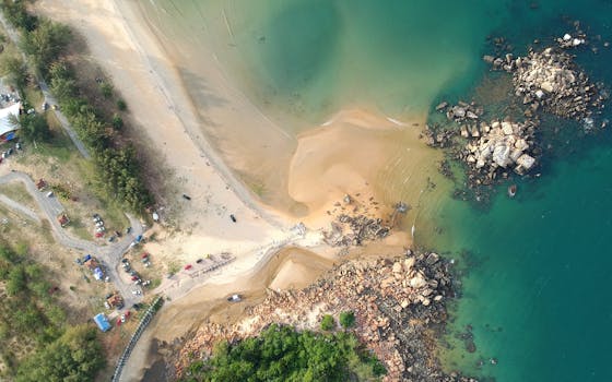 A stunning aerial shot of a sandy beach with clear turquoise waters and rocky formations.