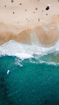 A top-down view of waves crashing onto a sandy beach, highlighting clear turquoise waters and golden sand.