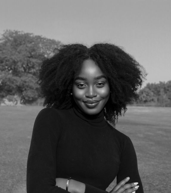 Striking portrait of a woman with afro hair smiling confidently in an outdoor setting.