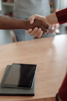 Close-up of a business handshake over a wooden table with a tablet, symbolizing agreement and technology.