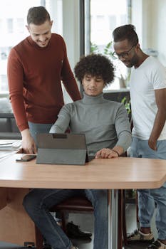 Three diverse colleagues working together on a tablet in an office, focusing on a shared screen.