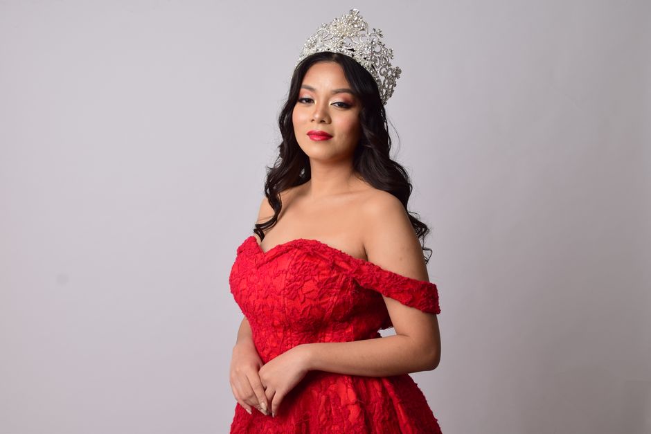 Portrait of an elegant woman wearing a red gown and tiara, posing indoors.