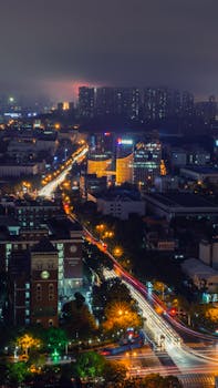 A bustling cityscape at night featuring illuminated buildings and vibrant street lights.