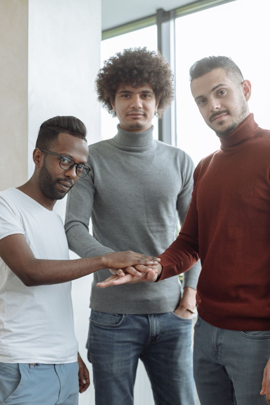 Três jovens homens diversos colaborando com as mãos juntas em um ambiente moderno de escritório.