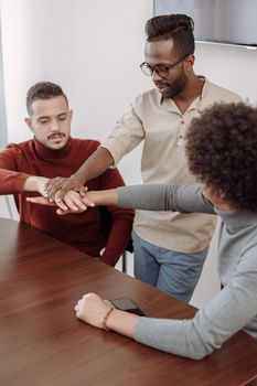 Three diverse adult colleagues collaborate with hands joined in an office meeting.