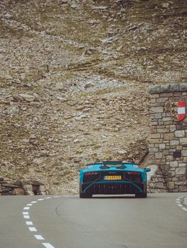 Rear view of a blue sports car on a winding mountain road, showcasing speed and luxury.