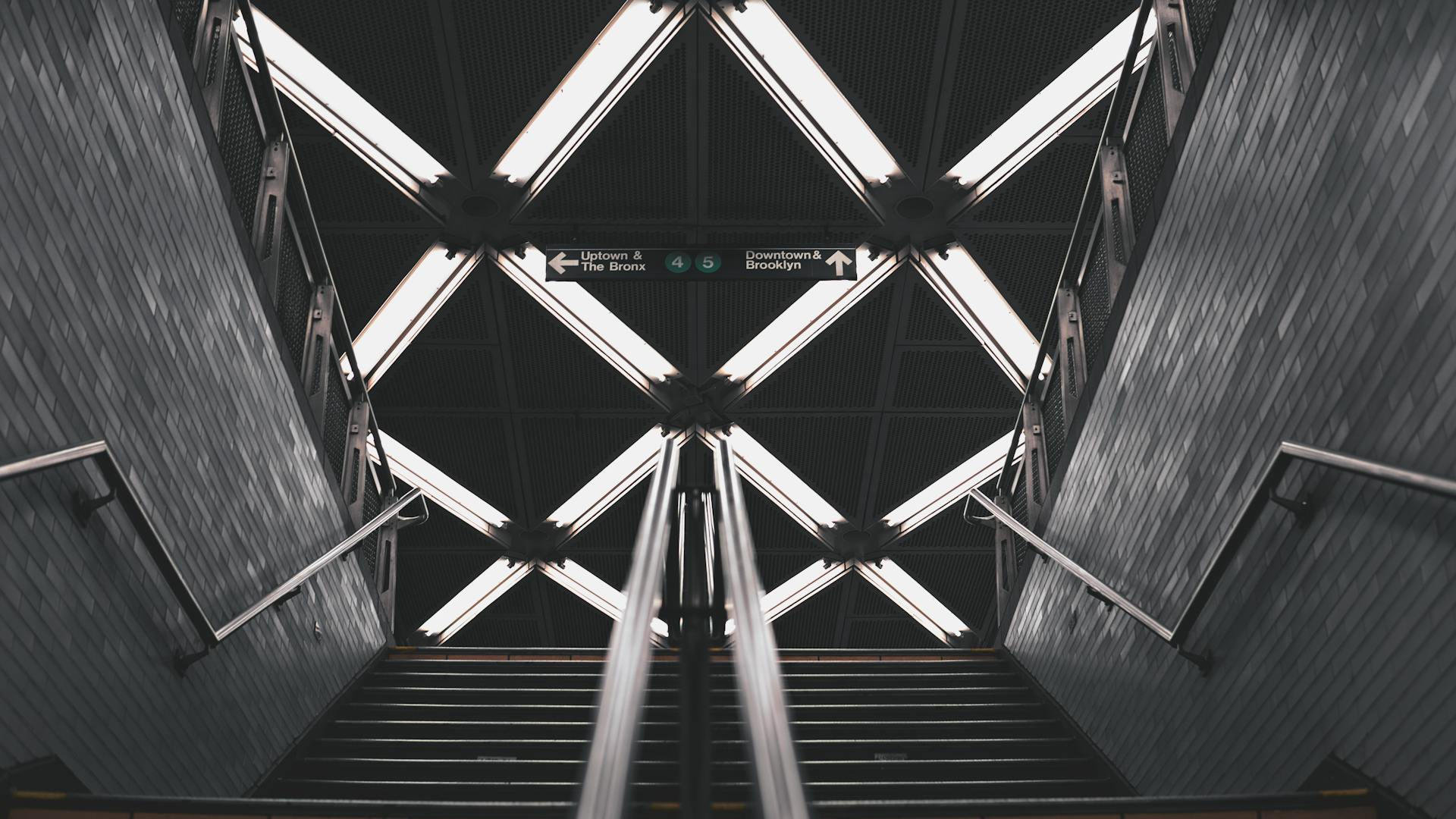 Dramatic view of subway station stairs in NYC with geometric ceiling lights.