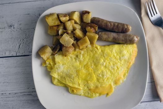 A hearty breakfast with omelette, browned potatoes, and sausages on a white plate.