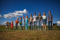 A diverse group of children and teenagers smiling under a sunny blue sky, showcasing unity and happiness.