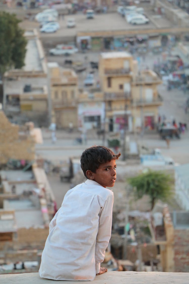 Boy In White Shirt Sitting On High Surface