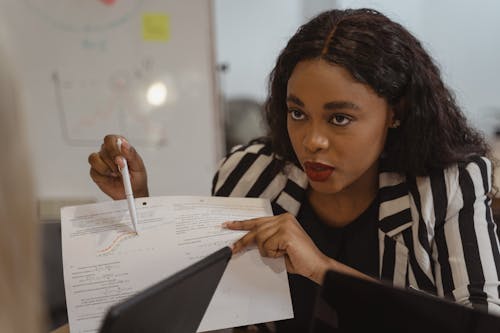 Woman in Black and White Blazer Pointing Her Pen on Paper 