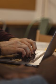 Close-up of hands typing on a laptop in an indoor setting with a blurred background.