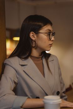一位女商人戴着眼镜、穿着西装外套，侧身坐在咖啡馆里