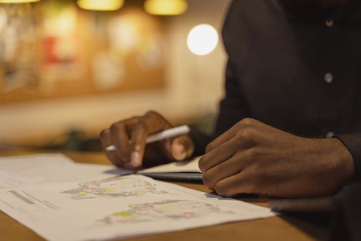A person writing on papers with pen at a desk indoors. Warm lighting creates a focused work environment.