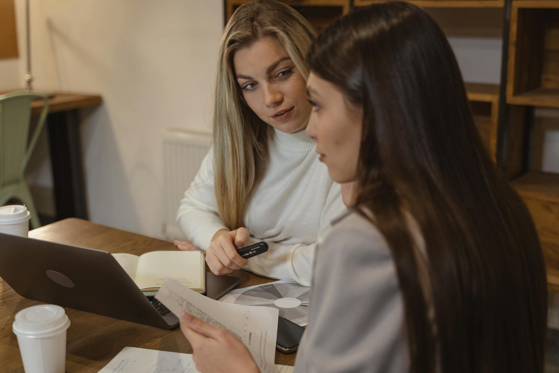 Two women in a modern office discussing business documents while sitting at a table.