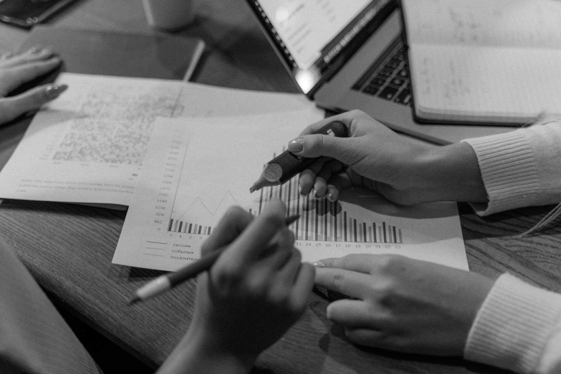 Monochrome image of hands analyzing documents and charts in an office setting.