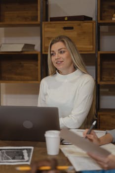 Young woman in casual meeting setting with laptop and coffee indoors.