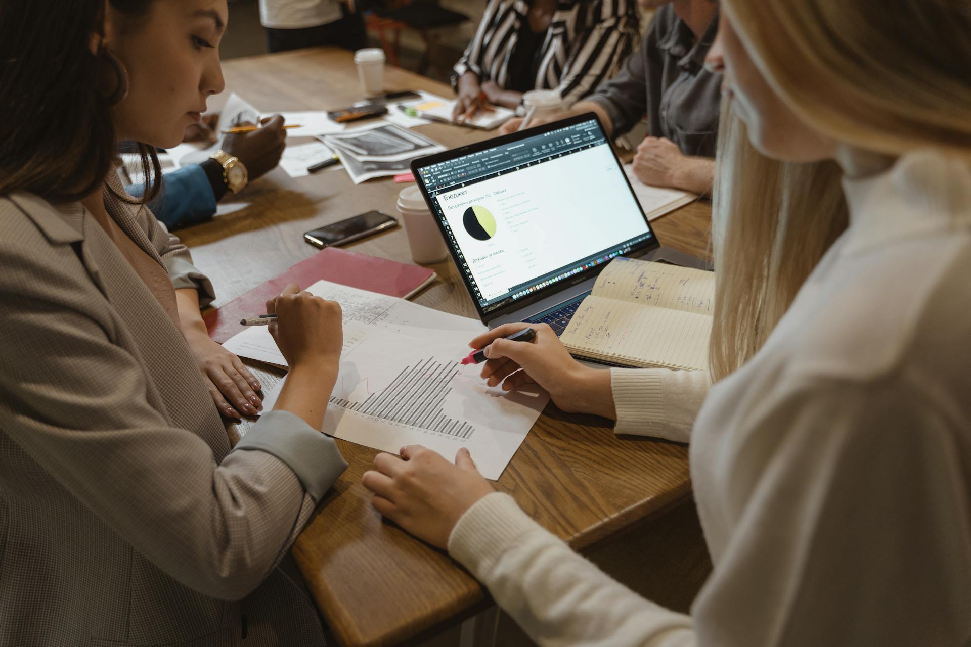 A diverse team collaborates on business strategy around a table with laptops and documents.