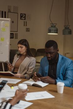 Diverse professionals collaborate in an office setting using smartphones and discussing work.