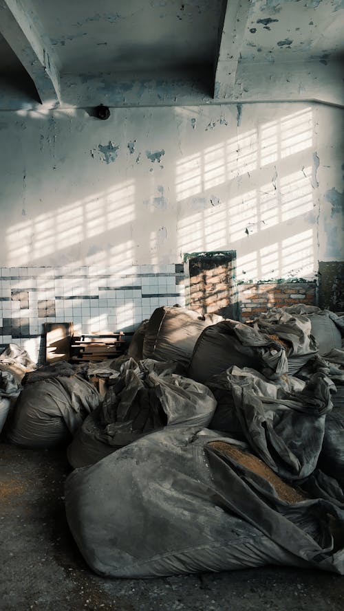 Aged abandoned house with cement walls and ceiling above pile of dirty bags in sunlight