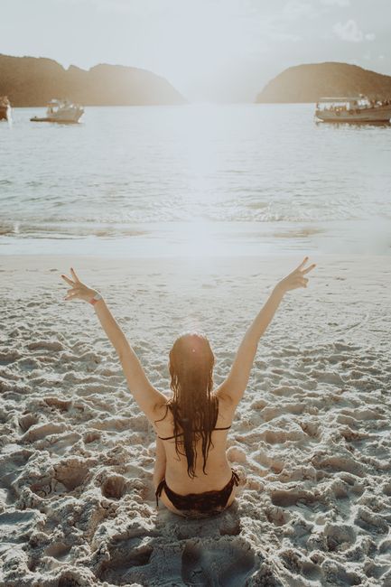 From above back view of anonymous female traveler with peace sign chilling on seashore in sunlight