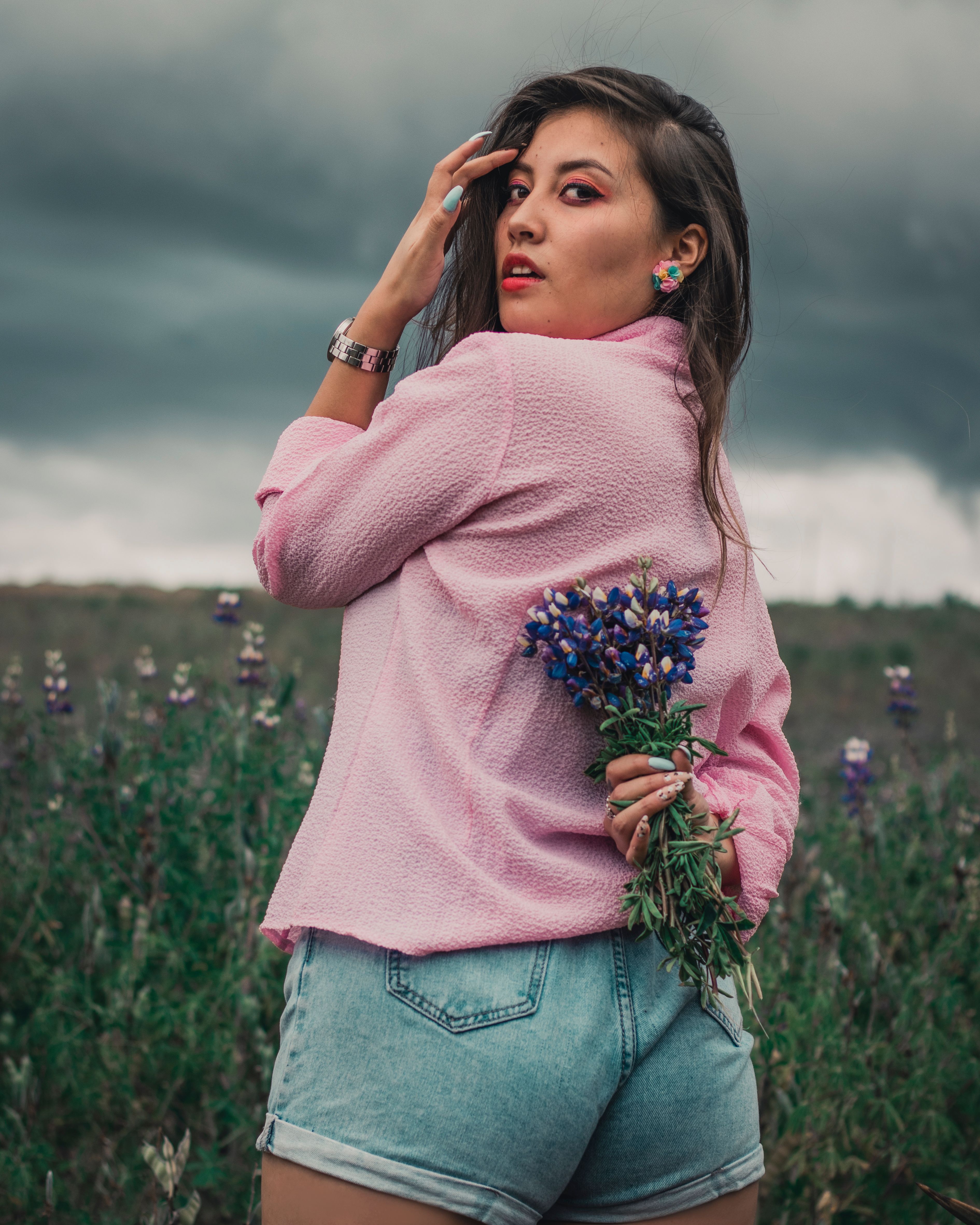 Fotomural Joven elegante sosteniendo flores moradas en un campo bajo un cielo nublado, Ecuador.