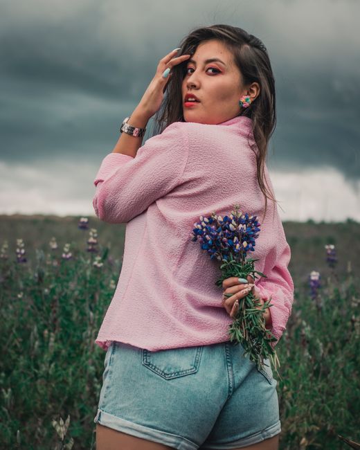 Fotomural Joven elegante sosteniendo flores moradas en un campo bajo un cielo nublado, Ecuador.