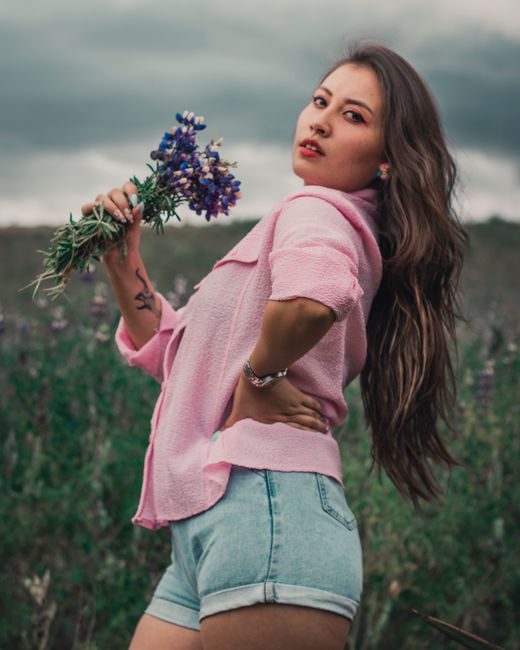 Fotomural Una joven posando con confianza al aire libre, sosteniendo un ramo de lavanda. Capturada en un entorno vibrante y natural.