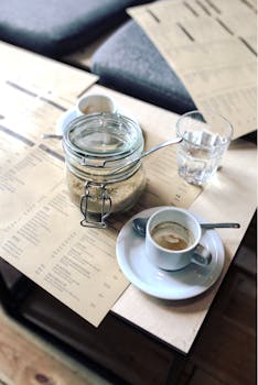 A warm coffee shop setting featuring espresso, sugar jar, menus, and glass on a table.
