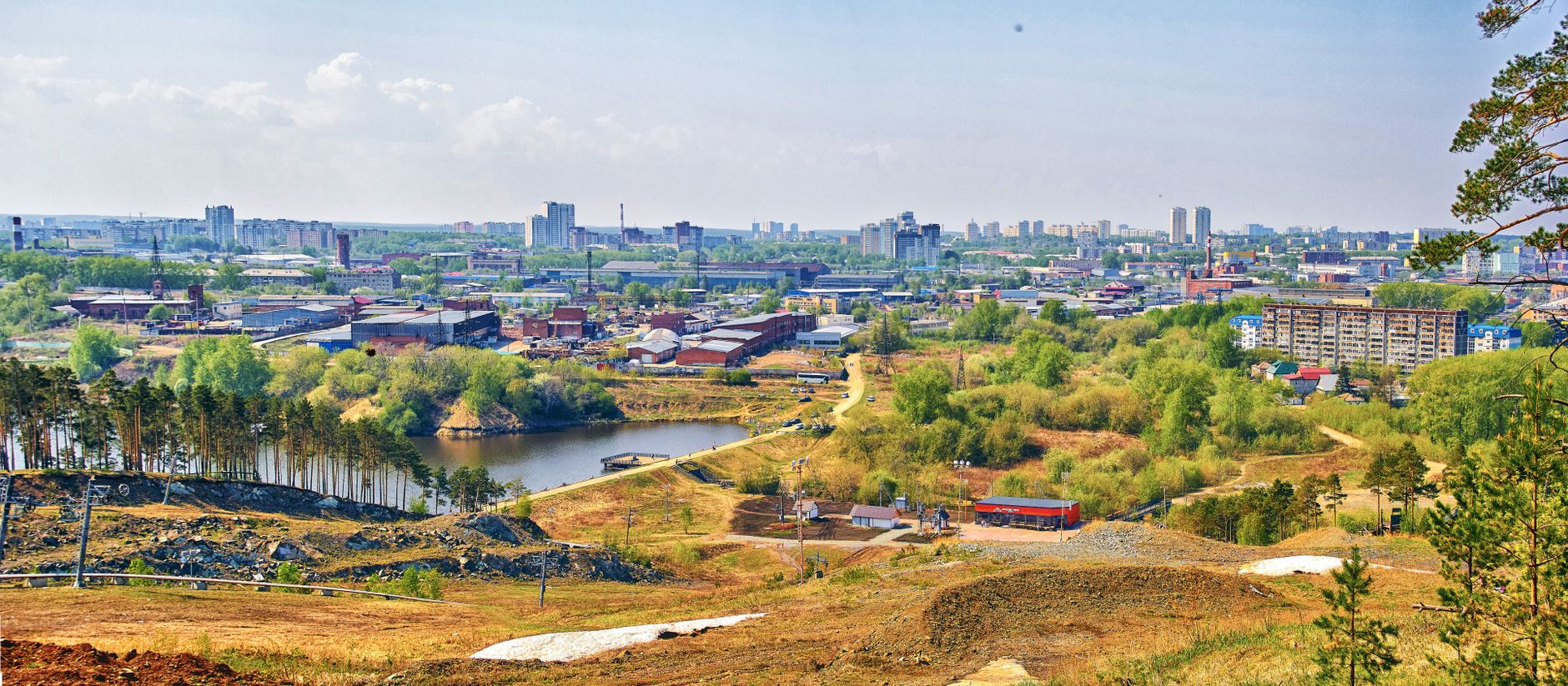 Panoramic aerial view of a cityscape with a lake, surrounded by lush greenery and urban architecture.