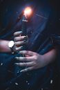 Unrecognizable female with dark manicure standing with black burning sparkling candle in hands during magic rite