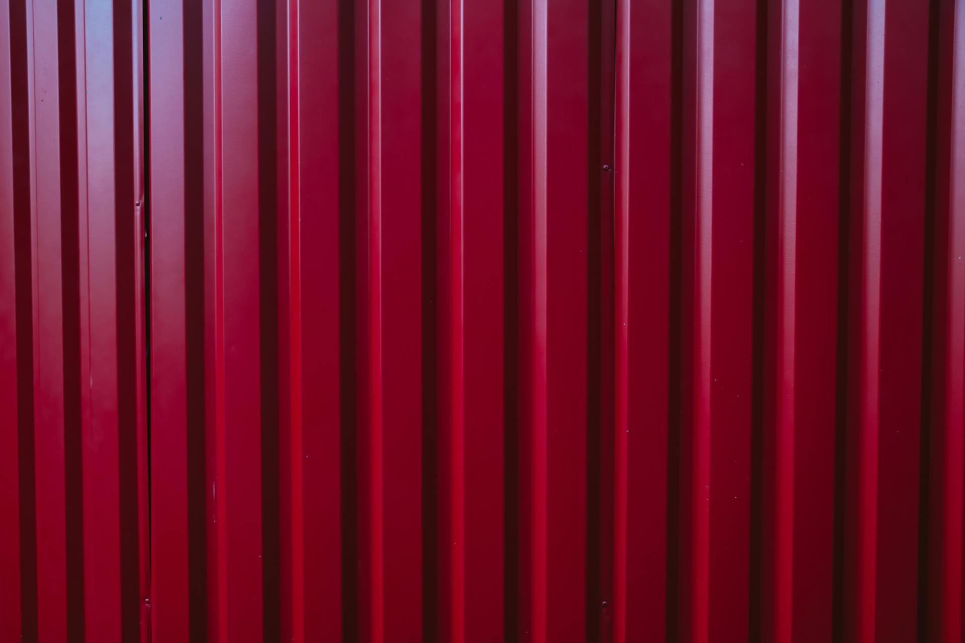Close-up of a red corrugated metal wall with vertical lines, perfect for backgrounds or patterns.