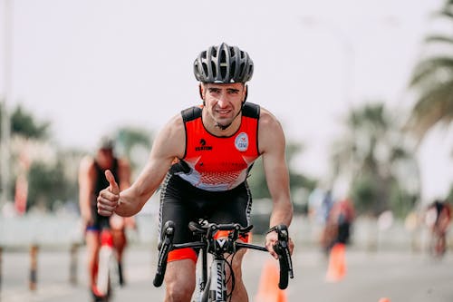 Muscular bicyclist with thumb up riding bike during competition