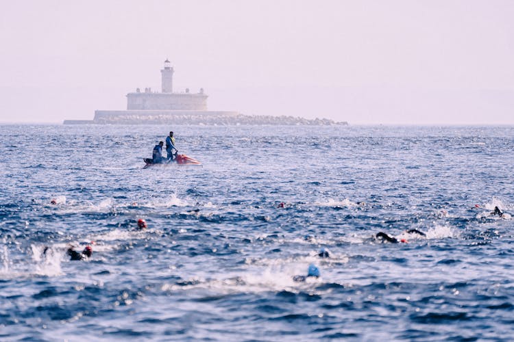 Unrecognizable Men On Powerboat On Wavy Sea Near Swimming Athletes