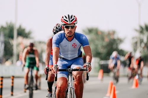 Serious male athlete in sportswear and helmet riding bicycle near anonymous competitors during race on roadway