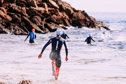 Back view of anonymous group of athletes in diving suits swimming in stormy sea near rock