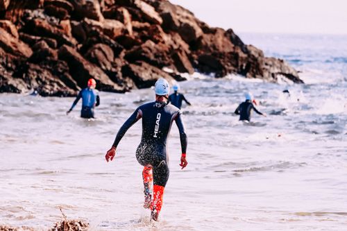 Free Back view of anonymous group of athletes in diving suits swimming in stormy sea near rock Stock Photo