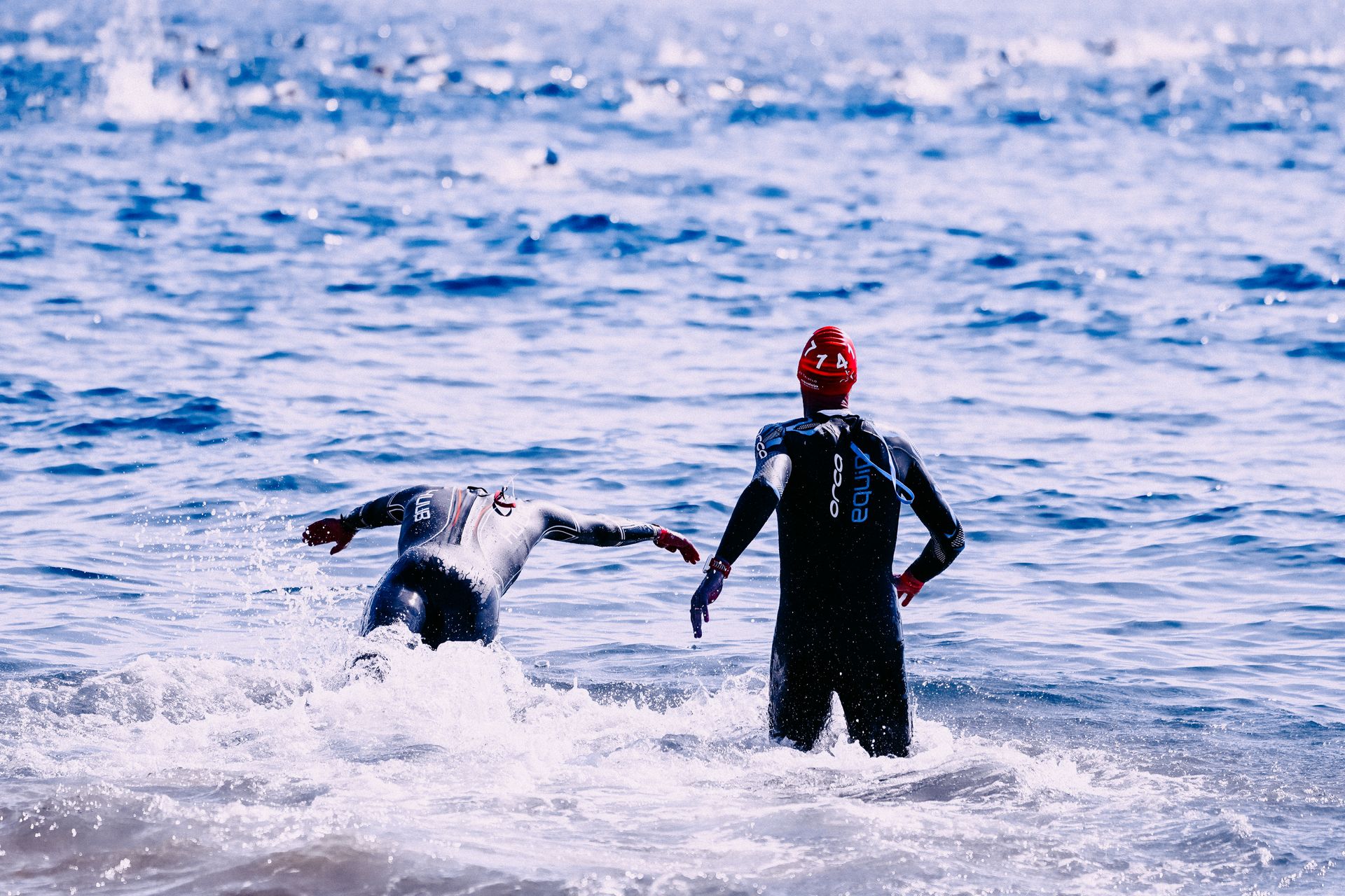 Two athletes in wetsuits dynamically competing in an open sea swim race.
