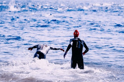 Free Back view of unrecognizable sportsmen in wet suits swimming in glowing wavy ocean with splashing water Stock Photo