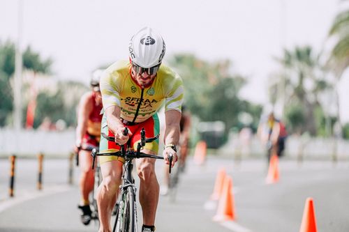 Free Fit male cyclist in sportswear and protective helmet riding bicycle behind anonymous competitors during race on road Stock Photo
