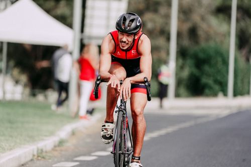 Free Cheerful muscular young sportsman in protective helmet riding bicycle on asphalt roadway while looking forward Stock Photo